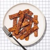 slices of tempeh bacon on white plate with black fork