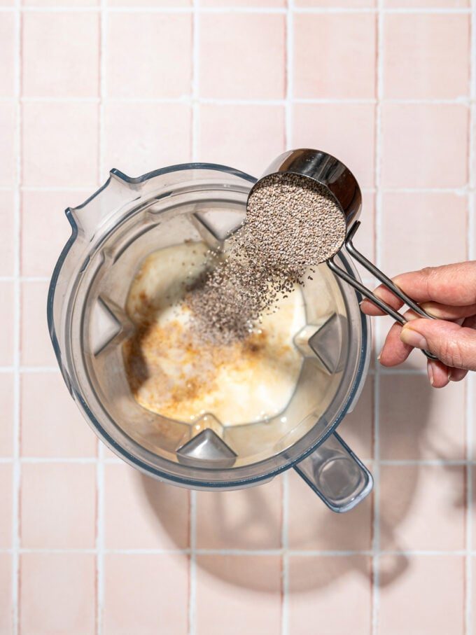 hand pouring chia seeds out of a measuring cup into blender