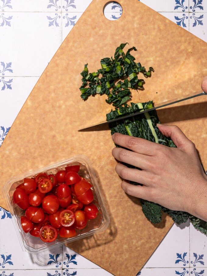 hand slicing green kale on cutting board with cherry tomatoes
