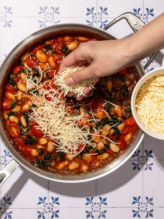 hand sprinkling vegan cheese shreds on pizza beans in skillet