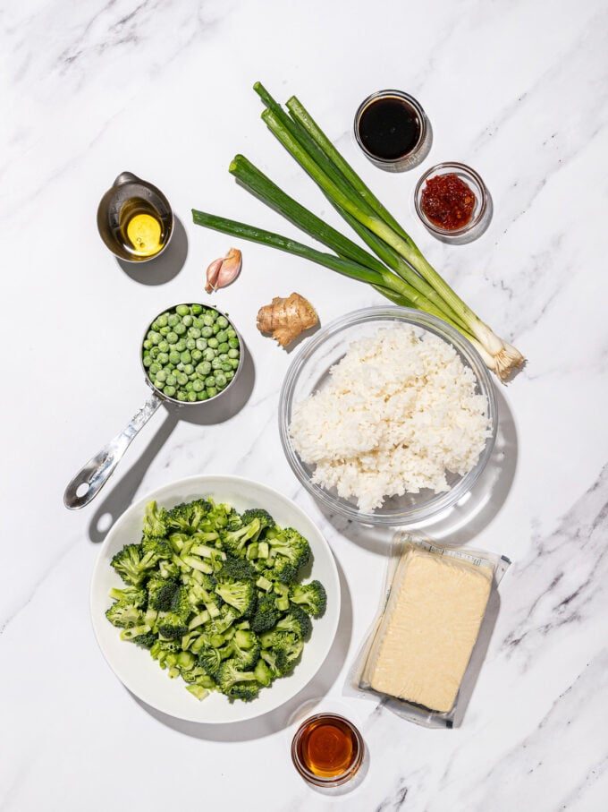 bowls of chopped broccoli, jasmine rice, frozen peas, a block of tofu and sauces 