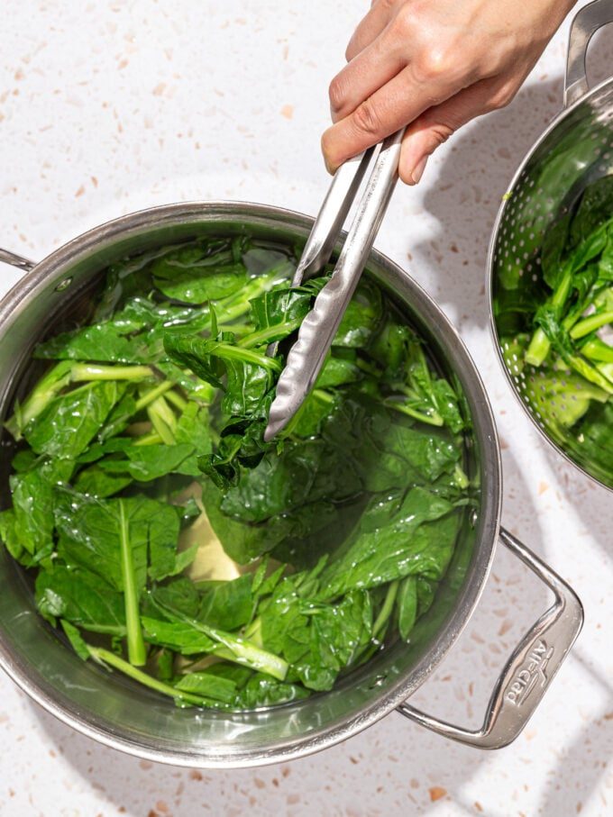 hand grabbing greens from pot with tongs