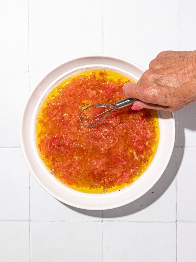 hand whisking grated tomato into olive oil