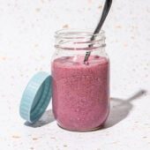 jar of raspberry blended chia pudding with spoon and blue jar lid beside