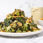 roasted broccoli with crumbled chickpeas piled high on a white plate with a glass jar of dressing and white bowl of chickpeas in the background