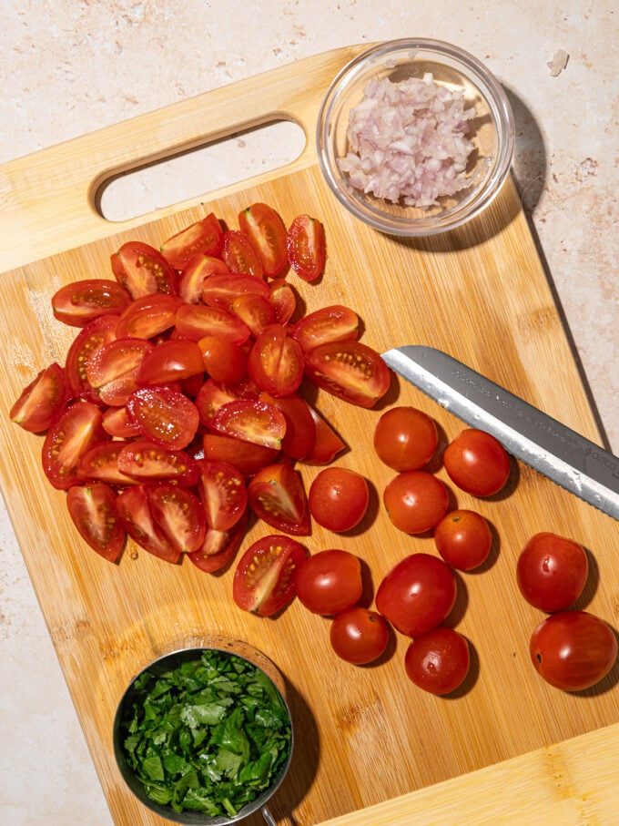 wooden cutting board with sliced cherry tomatoes, minced cilantro and shallot