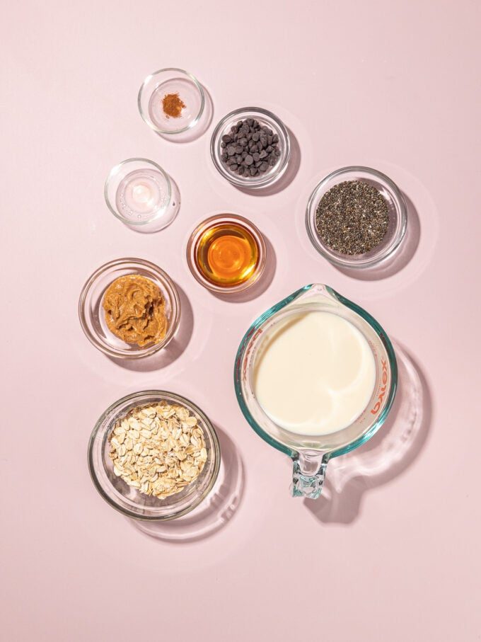 bowls of ingredients on a pink background: soy milk, chia seeds, rolled oats, peanut butter