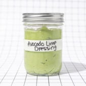 Glass jar of avocado lime dressing, labelled, on a black and white grid background
