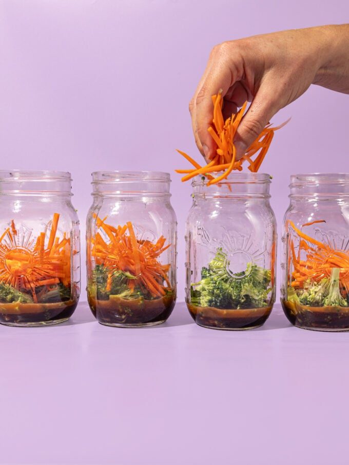 hand adding julienned carrots to glass jars