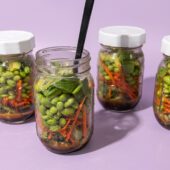 4 glass jars filled with edamame salad on a purple background