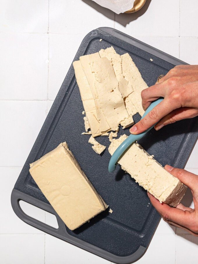 hand shaving tofu block with vegetable peeler